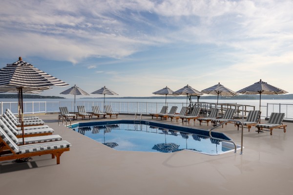 The image shows a poolside area with lounge chairs and striped umbrellas set against a scenic backdrop of water and sky, ending the sentence.