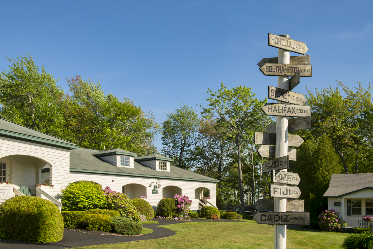 A scenic yard with buildings, manicured greenery, and a wooden signpost with multiple city names and distances pointing in various directions ends the sentence.