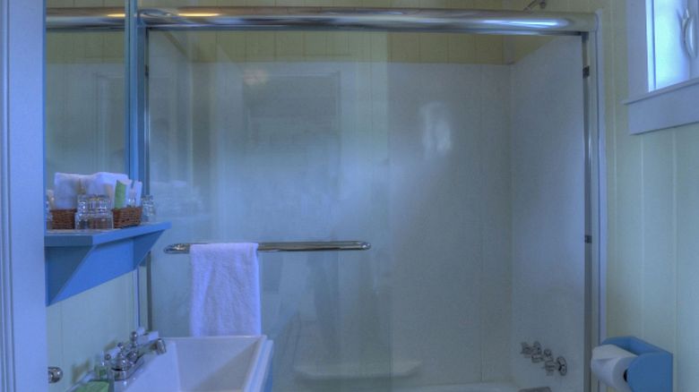 A bathroom with a shower-bathtub combo, blue vanity with sink, a wall mirror, wooden ceiling, towel rack, toilet, and a window above the toilet.