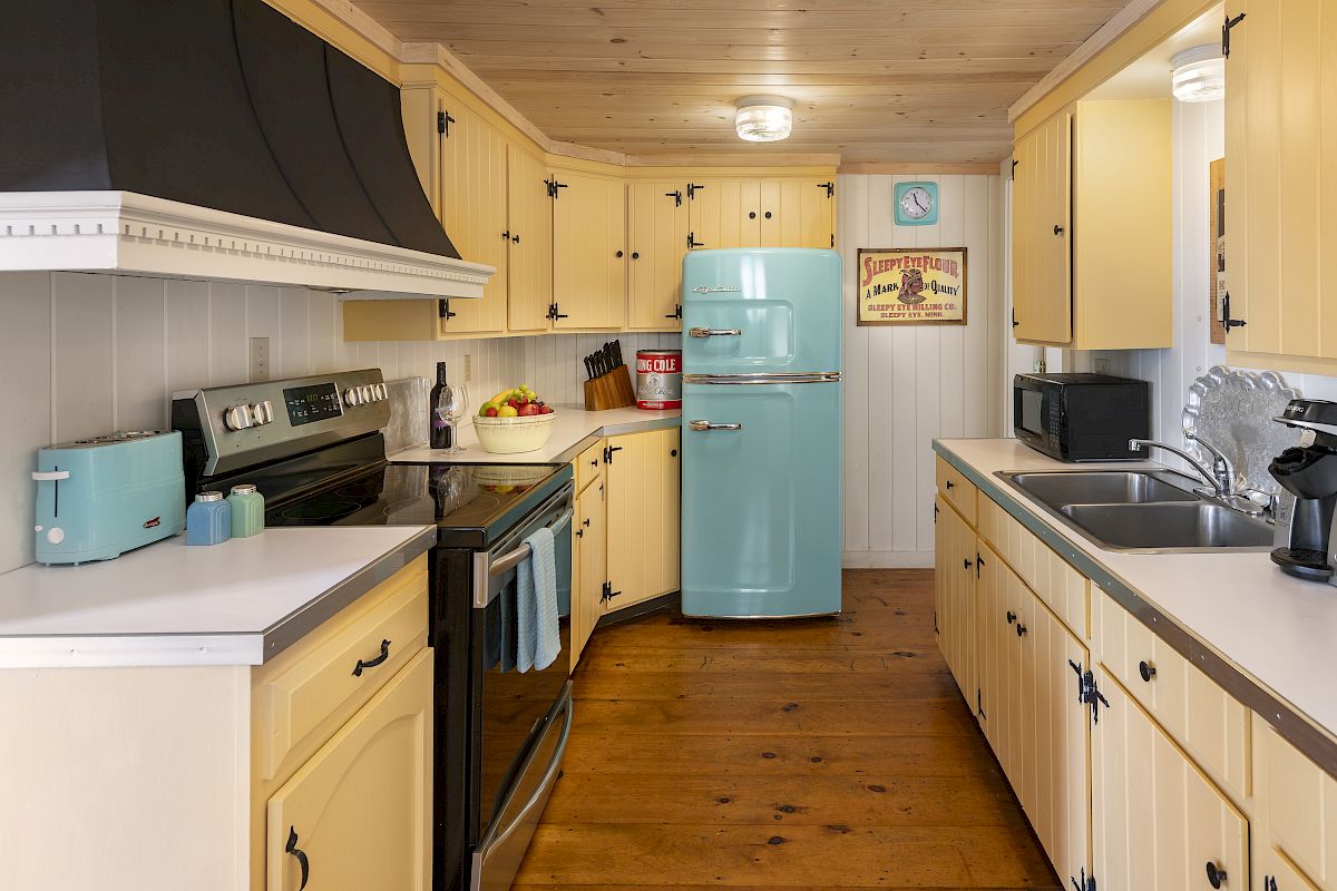 A cozy kitchen with yellow cabinets, a blue retro fridge, matching appliances, and wooden floors, creating a warm and nostalgic atmosphere.