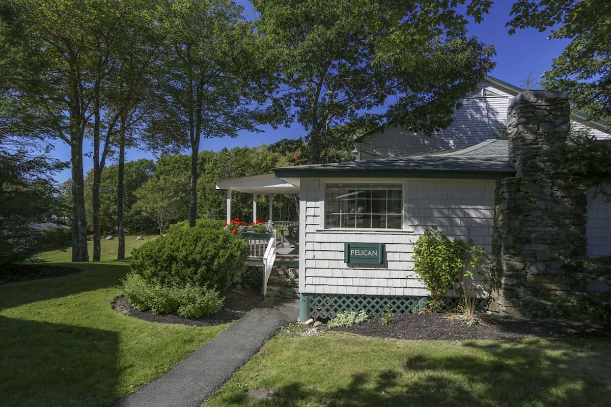 The image shows a house with a porch, surrounded by trees and greenery, with a sign reading