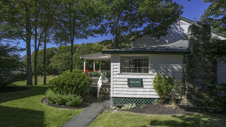 The image shows a house with a porch, surrounded by trees and greenery, with a sign reading 