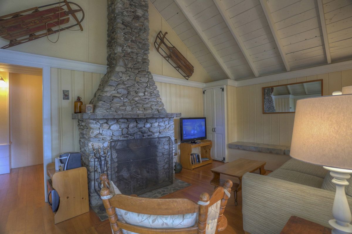 This image shows a cozy living room with a stone fireplace, wooden sleds on the wall, and a television. The room has high vaulted ceilings.