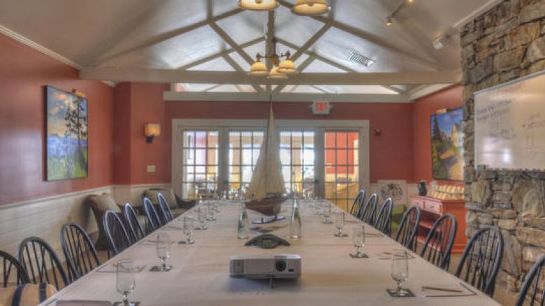 The image shows a conference room with a long table, chairs, a projector, water glasses, art on the walls, and a large window at the end of the room.