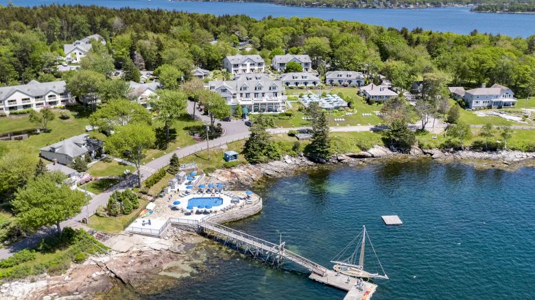 An aerial view of a waterfront resort with multiple buildings, a swimming pool, and a dock extending into the water amidst lush greenery.