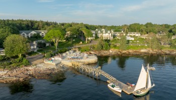 A coastal scene with a pier, boats docked, buildings and trees in the background, and calm waters reflecting the picturesque surroundings.