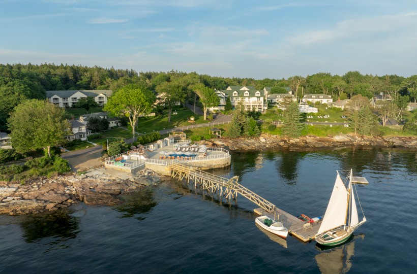 A coastal scene with a pier, boats docked, buildings and trees in the background, and calm waters reflecting the picturesque surroundings.