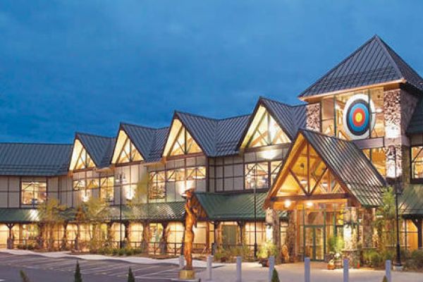 The image shows a large building with multiple peaked roofs, illuminated at night. There's a distinctive target symbol at the top, lit in the evening.