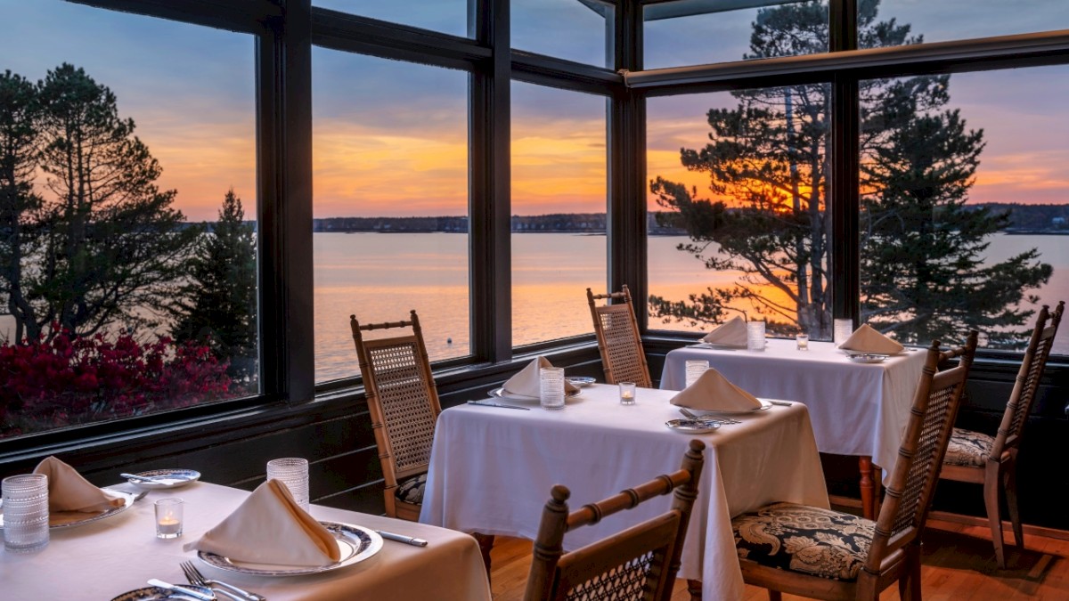 Restaurant with ocean view at sunset, tables set for dining.