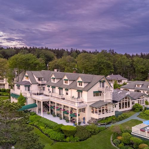 This image shows a scenic view of a large, elegant building with a well-maintained garden, set against a backdrop of trees and a purple sky.