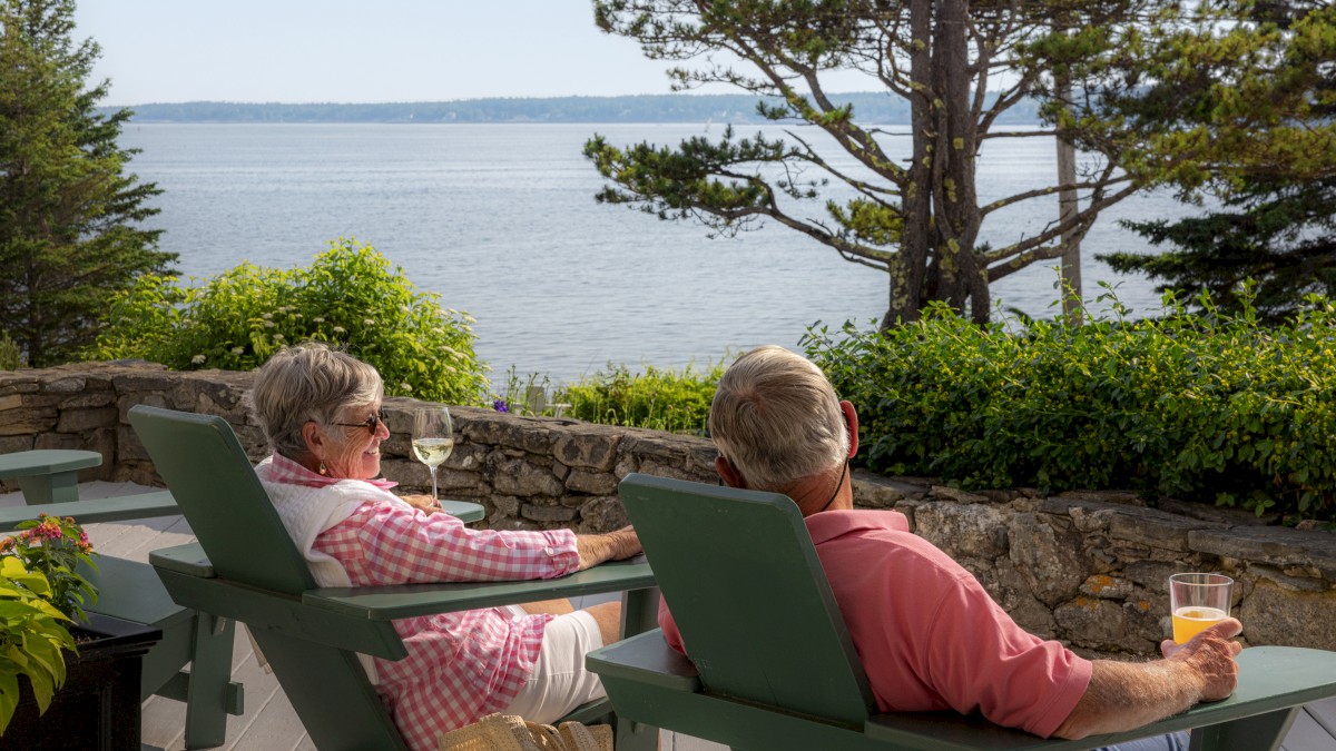 Two people relaxing in chairs with drinks, enjoying a scenic view of the ocean and trees.