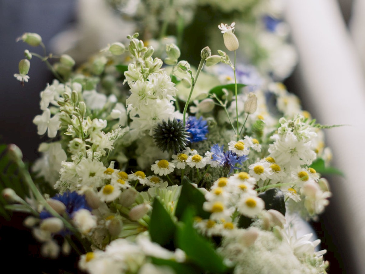 The image features a floral arrangement with white, yellow, and blue flowers, accented by green leaves and filler flowers.